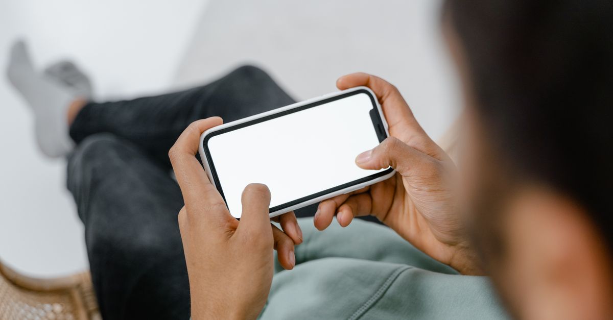 A person on a sofa checking a smart home app on a phone, the kind of app control the Shark vacuum vulnerability lets an attacker hijack remotely