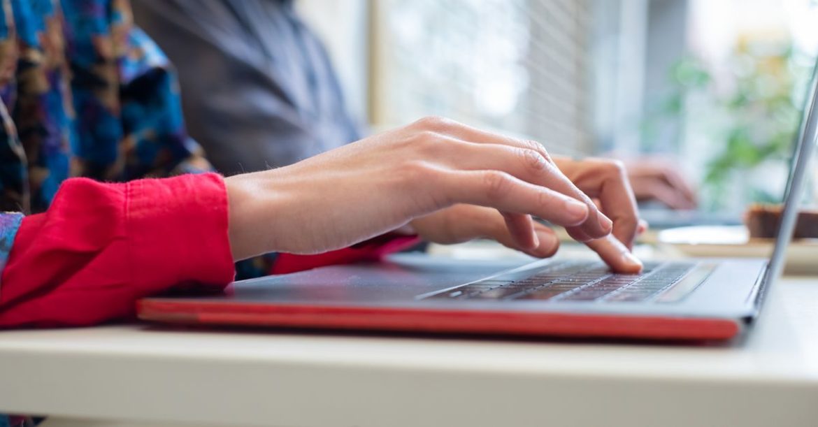 A person typing on a laptop keyboard in an office, illustrating the risk of opening a file affected by the 7-zip vulnerability