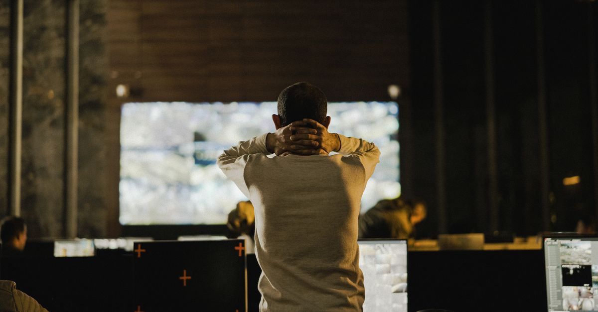 A security analyst facing a wall of monitors in a dim operations room, reviewing an incident
