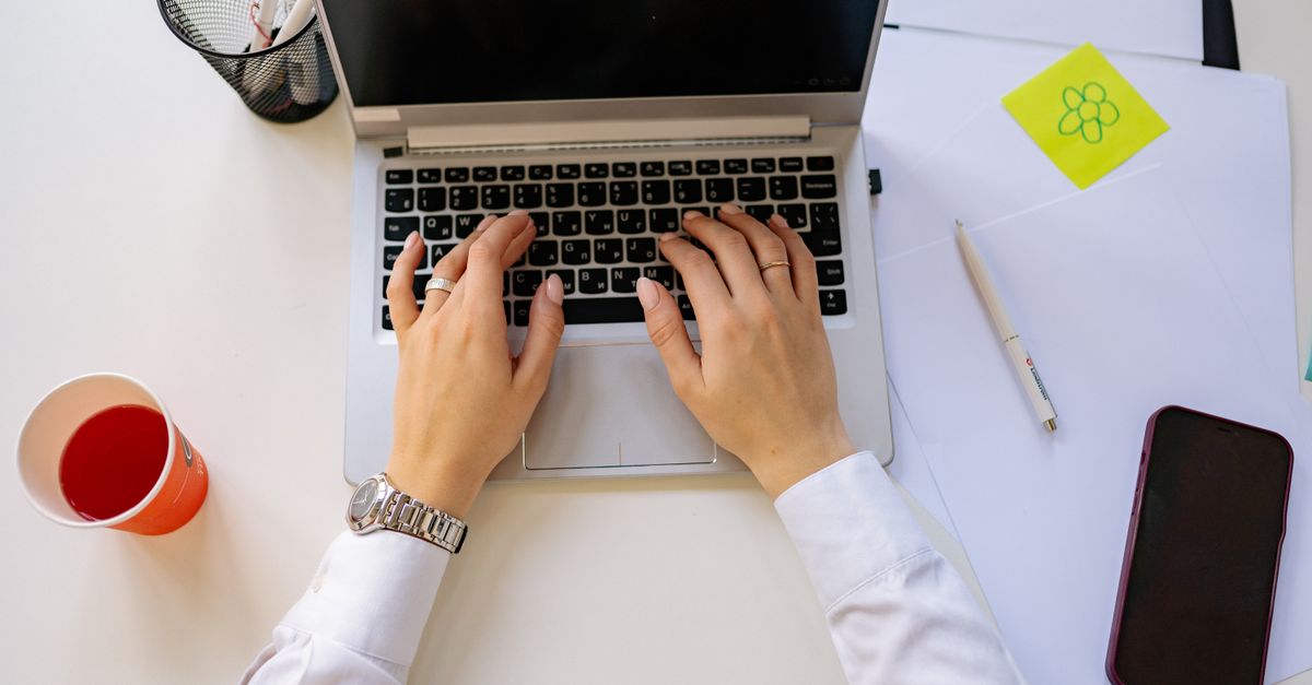 An overhead view of hands typing on a laptop at a desk, representing IT staff patching systems against the 7-zip vulnerability