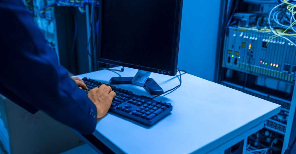 IT technician typing on a keyboard in a server room, the kind of login endpoint a credential stuffing attack targets