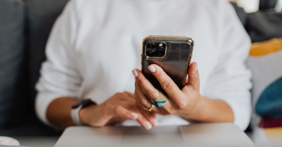 A hand holding a smartphone above a laptop, entering a code as part of a device code phishing attempt
